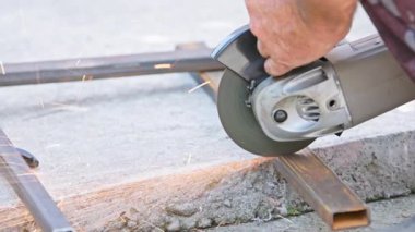 Çelik borular kesen bir adam var. Açık havada beton öğütücüyle. Gün içinde.