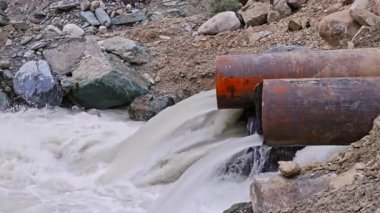 Dağ nehri suyu, çelik borular ve toprak seti kullanarak dağ nehri boyunca uzanan geçici boru köprüsünden akıyor.