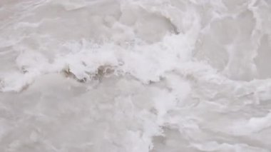 Çamurlu kaynayan suda sıkışan şeffaf plastik şişeler yavaş çekimde, tam kare arka planda.