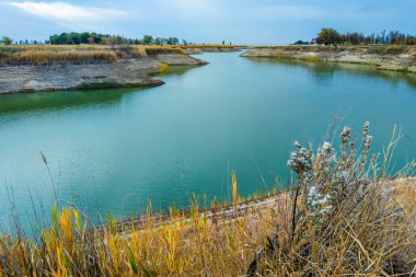 Sakin, turkuaz sularla çevrili kuru otlarla çevrili bir gölün huzurlu sonbahar manzarası. Su kaynakları, sonbahar güzelliği ve kırsal manzara konsepti.