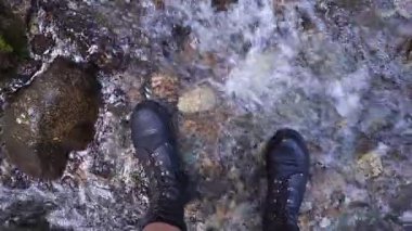 Ayak bileği çizmeli bacaklar sığ dağ deresinde yürüyüş yaparken yukarıdan gelen gonzo pov