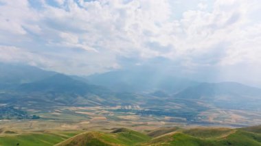 Güneşli bahar gününde, dağların önündeki çimenli yeşil tepelerin hava manzarası, parallax efektli kamyon kamerası hareketi.