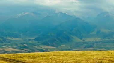 Sonbahar günü, uzak sisli bulutlu dağ sırasının önündeki kuru çim tepesi, kamyon kameralı hava manzarası.