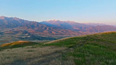 Uzak sisli bulutlu dağ sırasının önündeki yeşil çim tepesi sonbahar gündoğumunda, kamyon kameralı hava manzarası