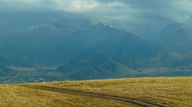 Sonbahar günü, uzak sisli bulutlu dağ sırasının önündeki kuru çim tepesi, kamyon kameralı hava manzarası.