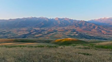 Uzak sisli bulutlu dağ sırasının önündeki yeşil çim tepesi sonbahar gündoğumunda, kamyon kameralı hava manzarası
