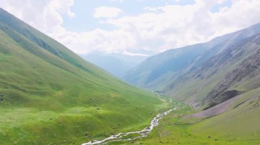 Kırgızistan 'da güneşli yaz gününde yeşil yamaçlı pitoresk dağ geçidi. Tian-Shan dağ sırasının üzerinde beyaz bulutlu mavi gökyüzü, Dolly ileri kamera hareketli drone bakış açısı.