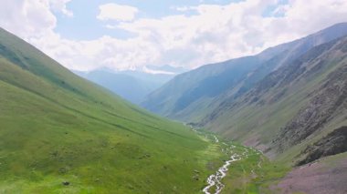 Kırgızistan 'da güneşli yaz gününde yeşil yamaçlı pitoresk dağ geçidi. Tian-Shan dağ sırasının üzerinde beyaz bulutlu mavi gökyüzü, Dolly ileri kamera hareketli drone bakış açısı.