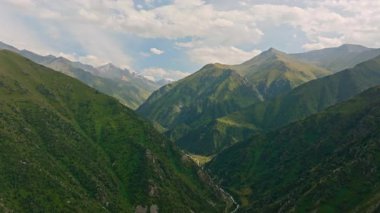 Gerçek zamanlı bir drone videosu Zhylamysh dağ vadisini, kıvrımlı bir nehir, yeşil yamaçlar ve Kırgızistan 'da parçalı bulutlu bir gökyüzünün altında zirvelerle yakalıyor..