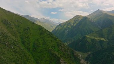 Gerçek zamanlı bir drone videosu Zhylamysh dağ vadisini, kıvrımlı bir nehir, yeşil yamaçlar ve Kırgızistan 'da parçalı bulutlu bir gökyüzünün altında zirvelerle yakalıyor..