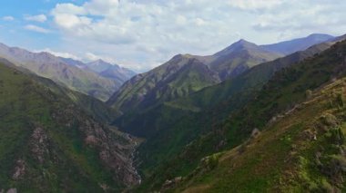 Gerçek zamanlı bir drone videosu Zhylamysh dağ vadisini, kıvrımlı bir nehir, yeşil yamaçlar ve Kırgızistan 'da parçalı bulutlu bir gökyüzünün altında zirvelerle yakalıyor..