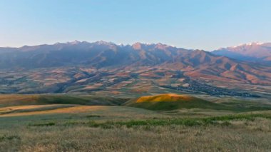 Sonbahar gündoğumunda, uzak sisli bulutlu dağ sırasının önündeki yeşil çimen tepesi, patlayan kamera hareketiyle hava manzarası
