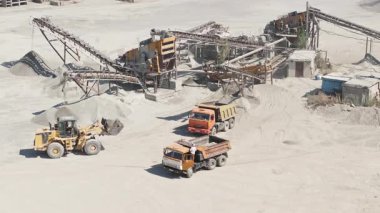 Taşıyıcı kayışlar, makineler ve Bişkek, Kırgızistan 'da 2 Ağustos 2024' te bir kamyona kum yükleyen ön uç yükleyici ile bir kum veya çakıl ezme alanının statik hava görüntüsü