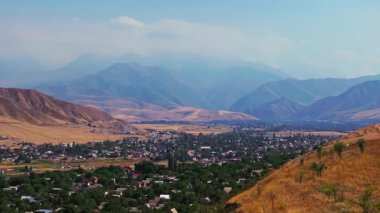 Kırgızistan 'da bir Bishkek banliyösünü görüntüleyen drone görüntüleri. Kuru Kırgız etekleriyle çevrili. İnsansız hava aracı köye doğru yavaşça ilerlerken uzak dağlarla dolu bir yaz sonu manzarası sergiliyor..