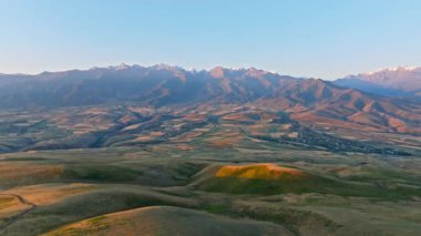 Sonbahar gündoğumunda, uzak sisli bulutlu dağ sırasının önündeki yeşil çimen tepesi, patlayan kamera hareketiyle hava manzarası
