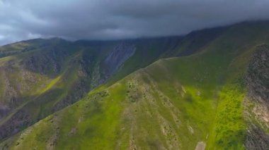 Bulutlu gökyüzünün altında yeşil yamaçları ve kayalık arazisi olan yemyeşil bir dağ vadisini ele geçiren hızlı bir iniş. Kamera yavaşça iniyor ve engebeli manzarayı gözler önüne seriyor..