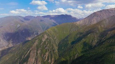 Kırgızistan 'ın engebeli dağ manzarasını gösteren hava aracı görüntüleri. Parçalı bulutlu gökyüzünün altındaki yeşil vadiler ve kayalık tepeler bölgenin doğal güzelliğini gözler önüne seriyor..