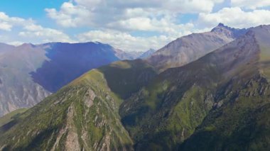 Kırgızistan 'ın engebeli dağ manzarasını gösteren hava aracı görüntüleri. Parçalı bulutlu gökyüzünün altındaki yeşil vadiler ve kayalık tepeler bölgenin doğal güzelliğini gözler önüne seriyor..