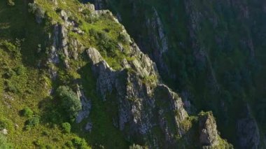 Kırgızistan 'daki dik, kayalık bir dağ uçurumunun hava drone görüntüsü yemyeşil ve dramatik bir arazi sergiliyor. Kamera soldan sağa hareket ediyor, parallax boyunca derinliği gösteriyor.