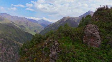 Bereketli yeşillikteki engebeli bir kayanın havadan görünüşü parçalı bulutlu bir gökyüzünün altında derin bir vadi ve uzak dağlar ortaya çıkarıyor. Soldan gelen bir dron tarafından yakalandı..
