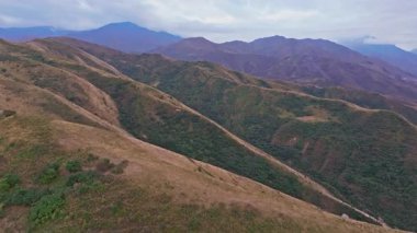 Kırgızistan 'daki Chu Vadisi' nin engebeli eteklerini görüntüleyen hava görüntüleri, kayan tepeleri, katmanlı dağları ve bulutlu gökyüzünü gösteriyor, kamera sürekli olarak doğal manzara üzerinde hareket ediyor..