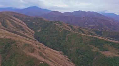 Kırgızistan 'daki Chu Vadisi' nin engebeli eteklerini görüntüleyen hava görüntüleri, kayan tepeleri, katmanlı dağları ve bulutlu gökyüzünü gösteriyor, kamera sürekli olarak doğal manzara üzerinde hareket ediyor..
