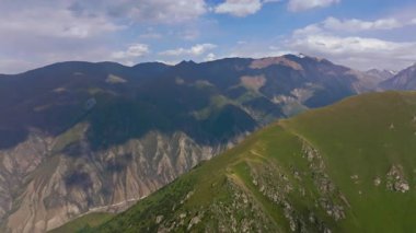 Kırgızistan 'ın engebeli dağ manzarasını gösteren hava aracı görüntüleri. Parçalı bulutlu gökyüzünün altındaki yeşil vadiler ve kayalık tepeler bölgenin doğal güzelliğini gözler önüne seriyor..