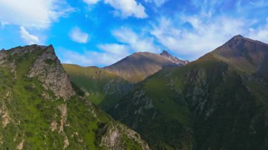 Akşamları engebeli dağları görüntüleyen hava görüntüleri yeşil vadiler, kayalık tepeler ve dağınık bulutlu açık mavi bir gökyüzü sergiliyor. Kamera ilerler, doğal manzarayı gözler önüne serer..
