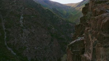 Drone görüntüleri, Kırgızistan 'daki bir dağ vadisinde kayalık bir kayalık kayalık kayayı yakalar. Dokusunu ve derinliğini, sola doğru pürüzsüz bir yay hareketiyle gözler önüne serer. Uzaktan kumlu, el değmemiş manzarayı gösterir..