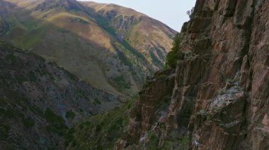 Drone görüntüleri, Kırgızistan 'daki bir dağ vadisinde kayalık bir kayalık kayalık kayayı yakalar. Dokusunu ve derinliğini, sola doğru pürüzsüz bir yay hareketiyle gözler önüne serer. Uzaktan kumlu, el değmemiş manzarayı gösterir..