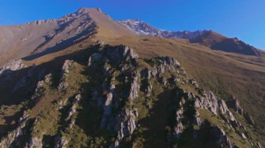 Kırgızistan 'daki kayalık bir dağ sırtının insansız hava aracı görüntüsü, kamerayı aşağı eğerken yukarı hareket ediyor, merkezdeki kayalık yüzeyi koruyor..
