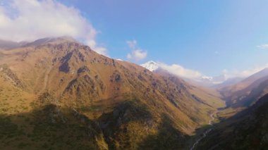 Kırgızistan 'da güneşli bir günde bulutlu ve karla kaplı sonbahar dağlarının hava manzarası.