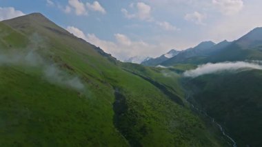 Kırgızistan, Chunkurchak Boğazı 'nda yaz mevsiminde beyaz bulutlu yeşil dağların insansız hava aracı görüntüsü. Kamera hareketini arttır.