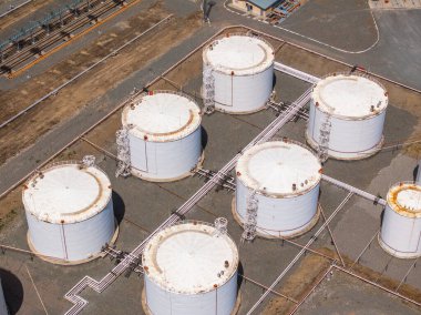 Seven large white storage tanks stand prominently at an industrial site. The bright daylight highlights the utilitarian design and structure of the tanks, creating an industrial mood.