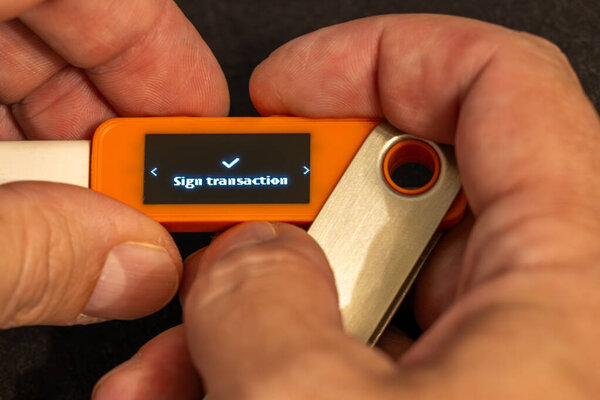 man with light skin signing a transaction using orange hardware wallet with small screen