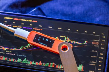 Hardware wallet prominently displays Ethereum cryptocurrency alongside a tablet showing price chart.