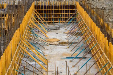 Construction site features wooden formwork and metal rebar, highlighting ongoing work. Daytime setting captures industrial mood of unfinished structure.