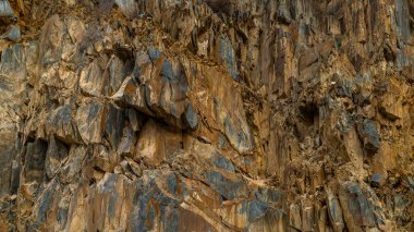 Rugged brown sedimentary cliff, full-frame closeup during daytime in Kyrgyzstan.
