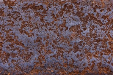 Rough metal surface displays significant rust and corrosion in an outdoor industrial environment. Daytime lighting accentuates the aged texture and weathered appearance.
