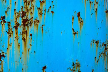 Weathered metal surface displays rust and peeling paint under bright daylight. Outdoors in an industrial setting, capturing a rustic and aged mood.