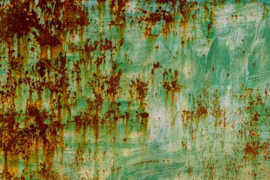 Textured metal surface displays signs of rust and peeling paint in an outdoor industrial environment. Daytime light reveals weathered details, evoking a sense of age and history.