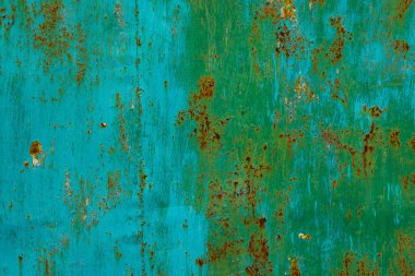 Rusty metal surface displays significant corrosion and peeling green paint in an industrial outdoor setting. The grunge aesthetic evokes a sense of age and weathering under bright daylight.