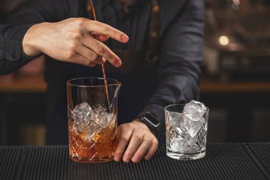 Barın tezgahında ezilmiş buz ve rom ile şeffaf bardakta barmen kokteyli karıştırıyor.