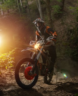 Motosikletli bir sporcu zor bir orman bölgesinde bisiklet sürüyor.