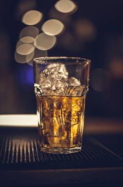 Bir bardak viski buzlu kayaların üzerinde siyah bir bar paspasına konmuş.