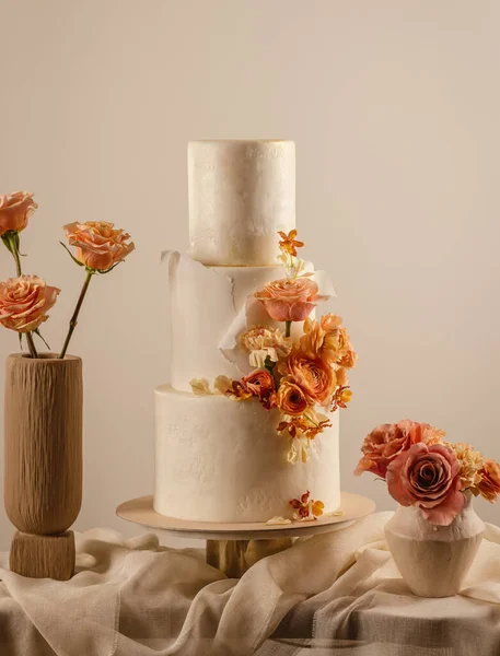 Peach fuzz coloured wedding cake decorated by flowers standing on table