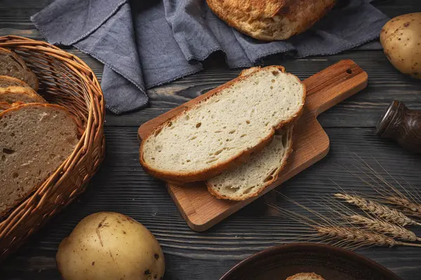 切菜板上的新鲜切碎的乡村面包 配上土豆和小麦 放在深色的木材表面上 图库图片