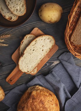 Rustic setup of freshly baked bread, potatoes, and wheat ears on a dark wooden background clipart