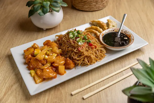 एशियाई व्यंजन जिसमें सॉस के साथ नूडल्स, डंपलिंग और मीठे और खारा चिकन शामिल हैं स्टॉक तस्वीर