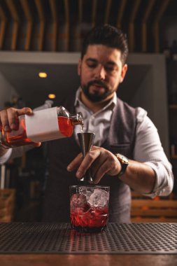 Yetenekli erkek barmen dikkatli bir şekilde süzgeçten geçen kırmızı bir kokteyli bardağa dolduruyor.